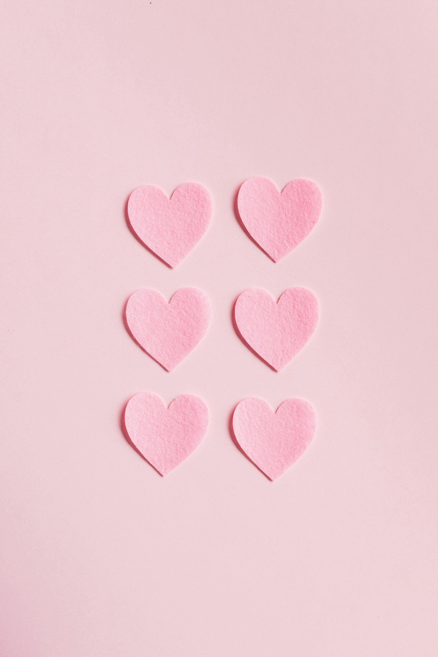 Soft pink heart shapes on a light pink background, perfect for romantic themes.